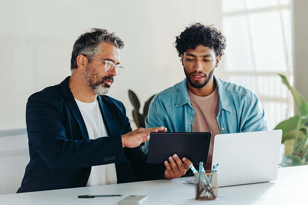 A businessman sitting by the window using his iPad, representing grenke's commitment to providing fast and flexible leasing solutions, sending payments within 24 hours to align with resellers' strategic goals.